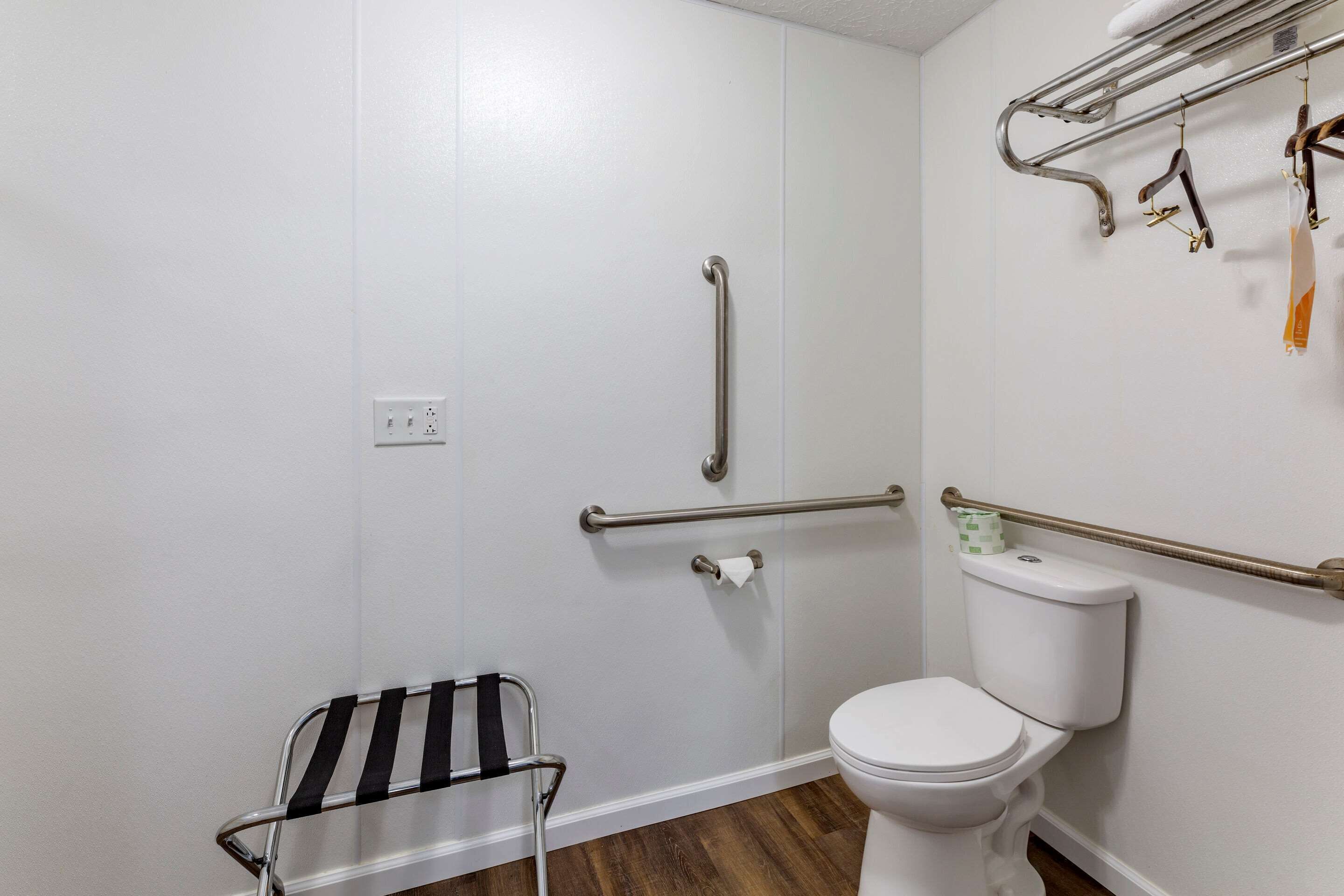 Une salle de bain avec des toilettes blanches, un espace douche équipé d’une barre d’appui et un porte-serviettes avec des serviettes.