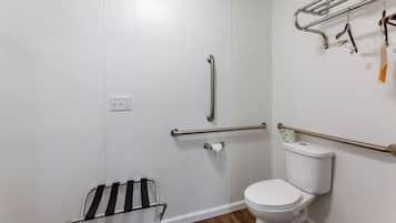 Une salle de bain avec des toilettes blanches, un espace douche équipé d’une barre d’appui et un porte-serviettes avec des serviettes.
