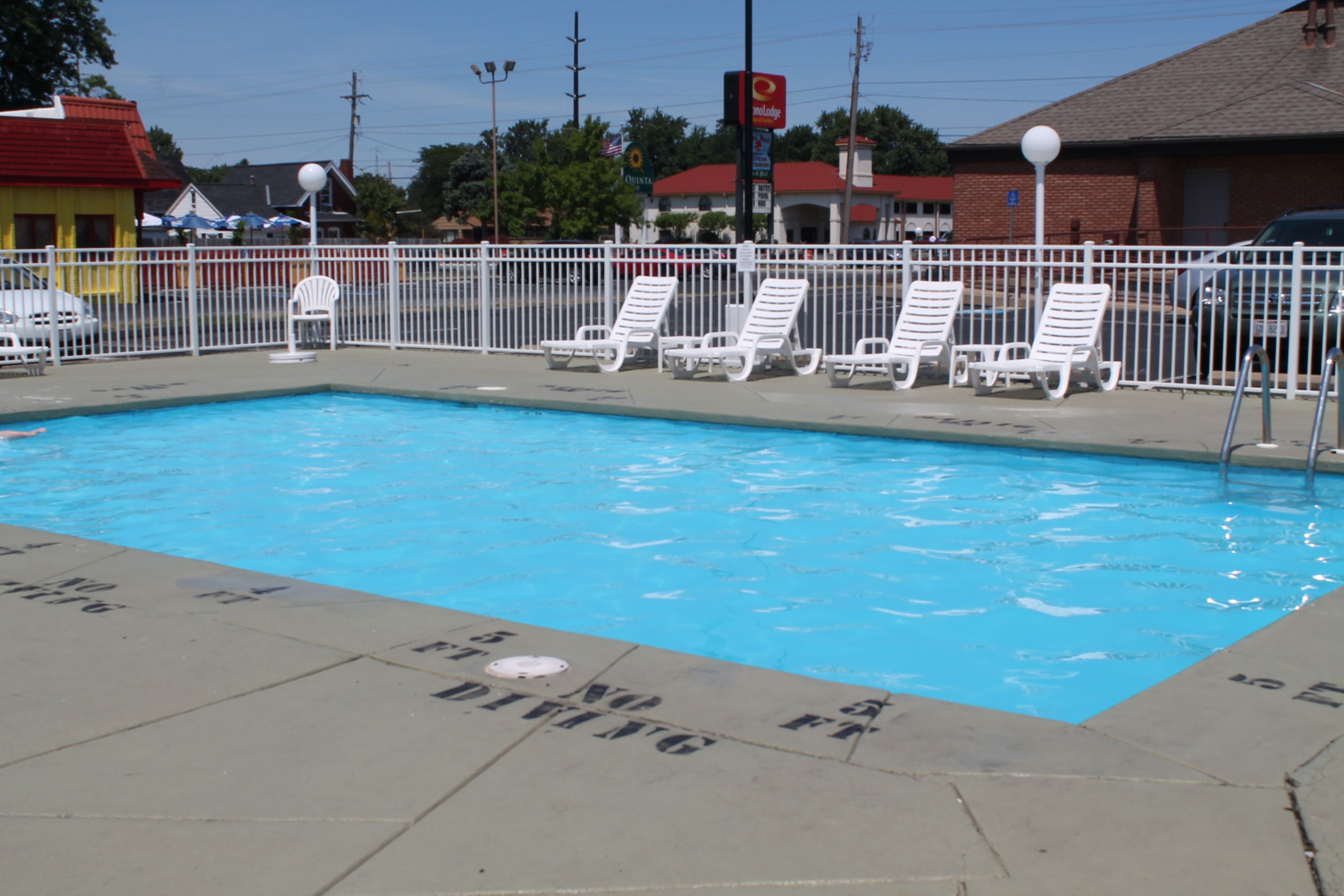 A swimming pool with white lounge chairs and a white fence.