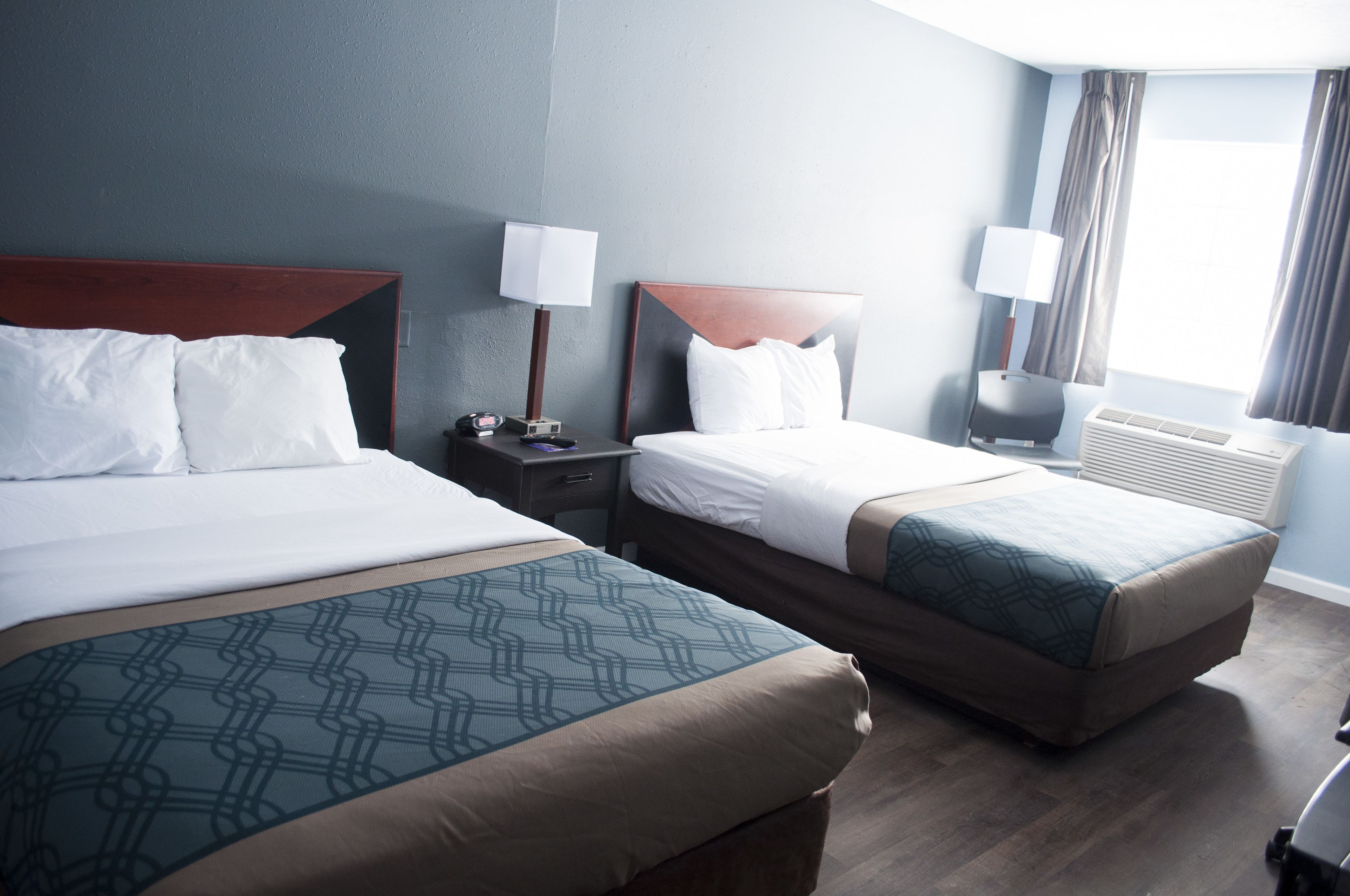 A hotel room with two beds, a nightstand, a lamp, and a window with curtains.