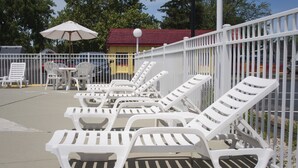 White lounge chairs and a table with chairs, a white fence, and a red-roofed building in the background. - Econo Lodge Inn & Suites Sandusky South (Sandusky)