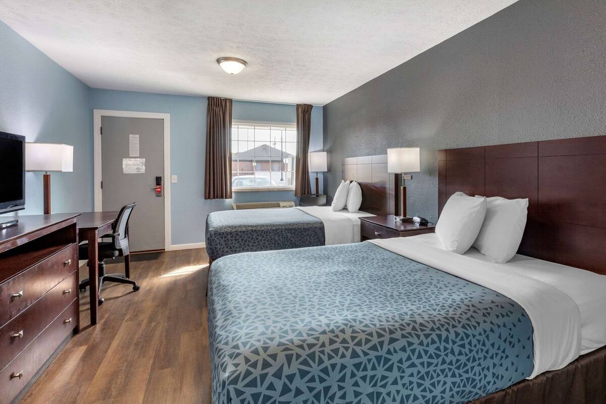 A hotel room with two beds, a desk with a chair, a television, and a window with curtains.