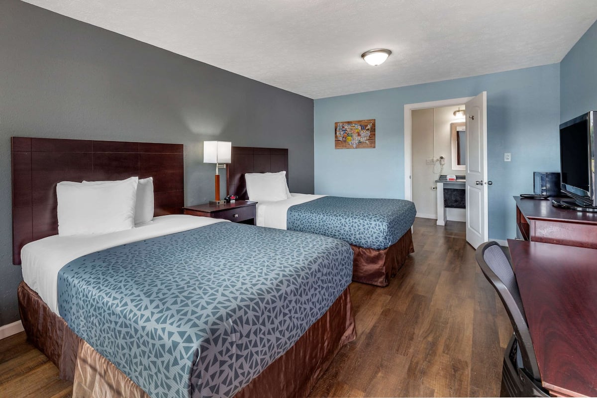A hotel room with two beds, a desk, a chair, a TV, and a bathroom visible through an open door.