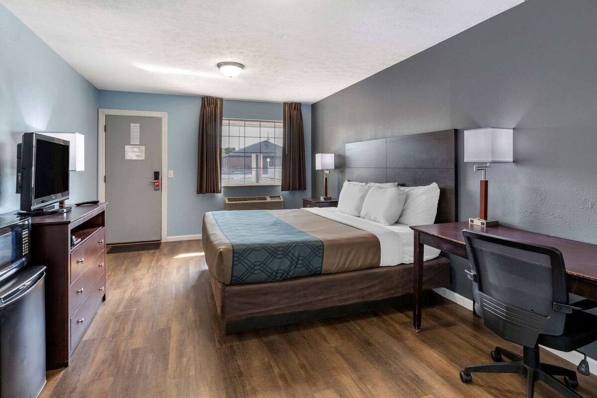 A hotel room with a bed, desk, chair, television, and a window with curtains.