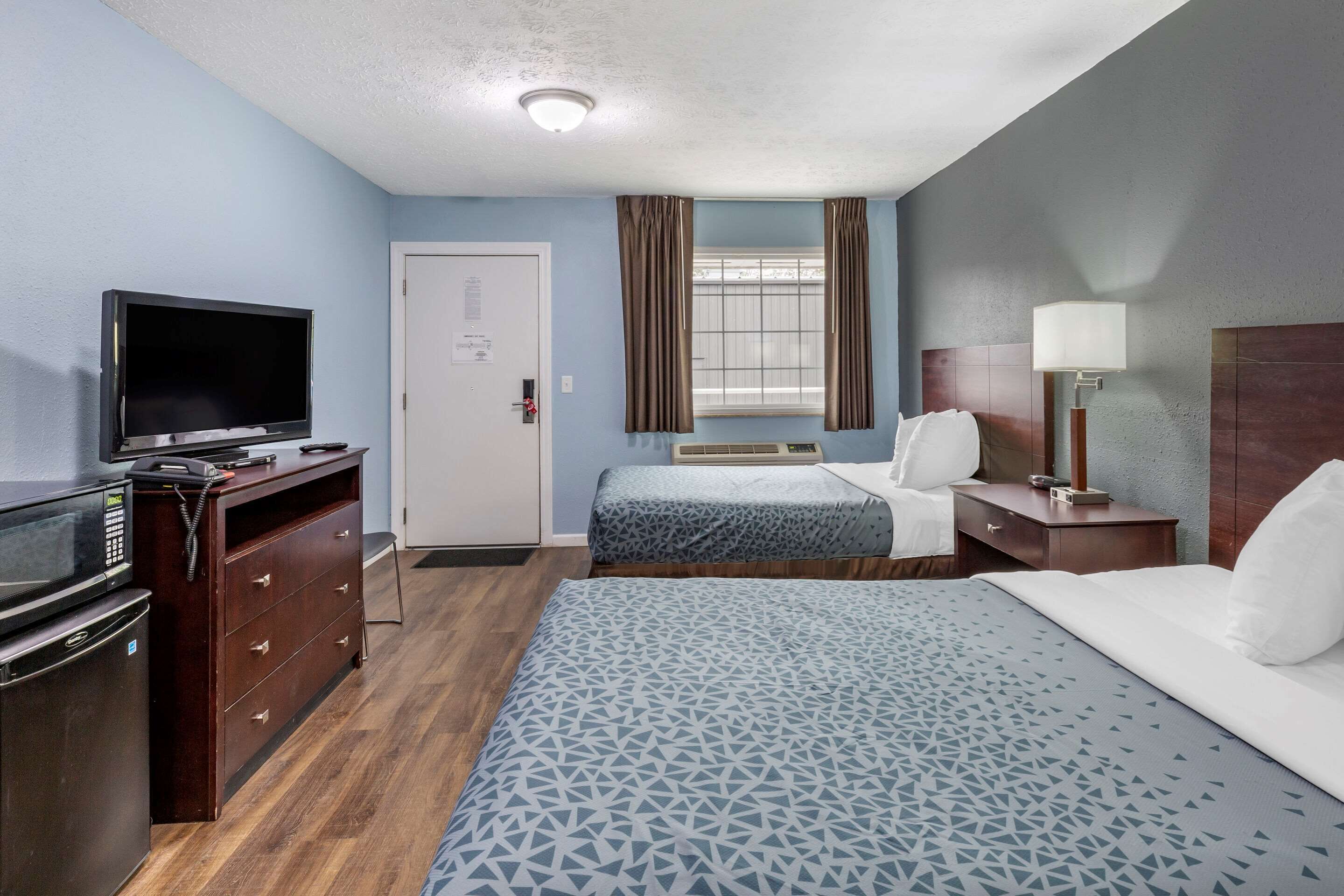 Una habitación de hotel con cama, escritorio, televisor, armario y ventana con cortinas.