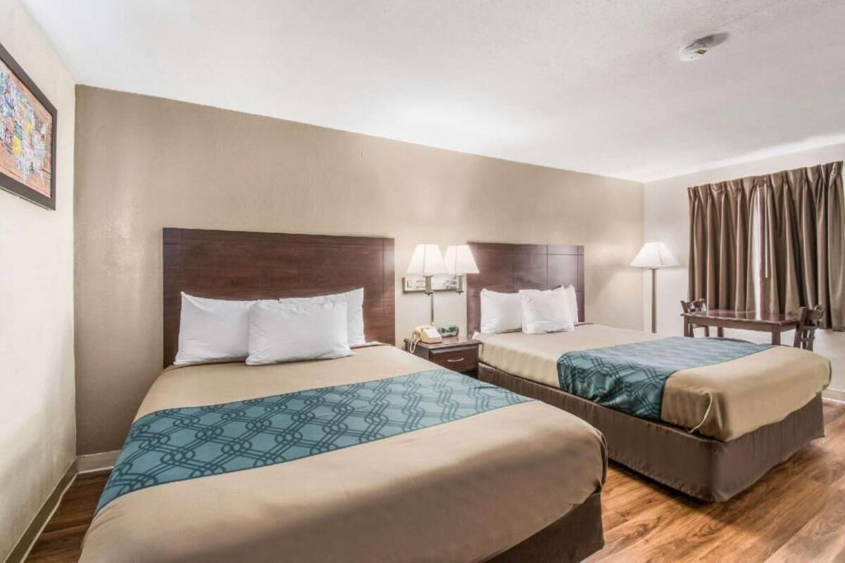 Habitación de hotel con dos camas, un escritorio, una silla y una ventana con cortinas.