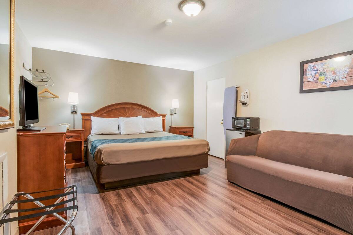 Habitación de hotel con cama, sofá, escritorio con televisor, lámpara y un mapa en la pared.