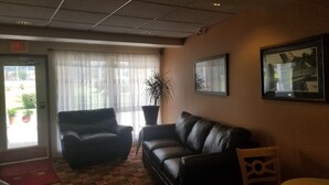 A lobby with a black leather sofa, a chair, a potted plant, and a framed picture on the wall.