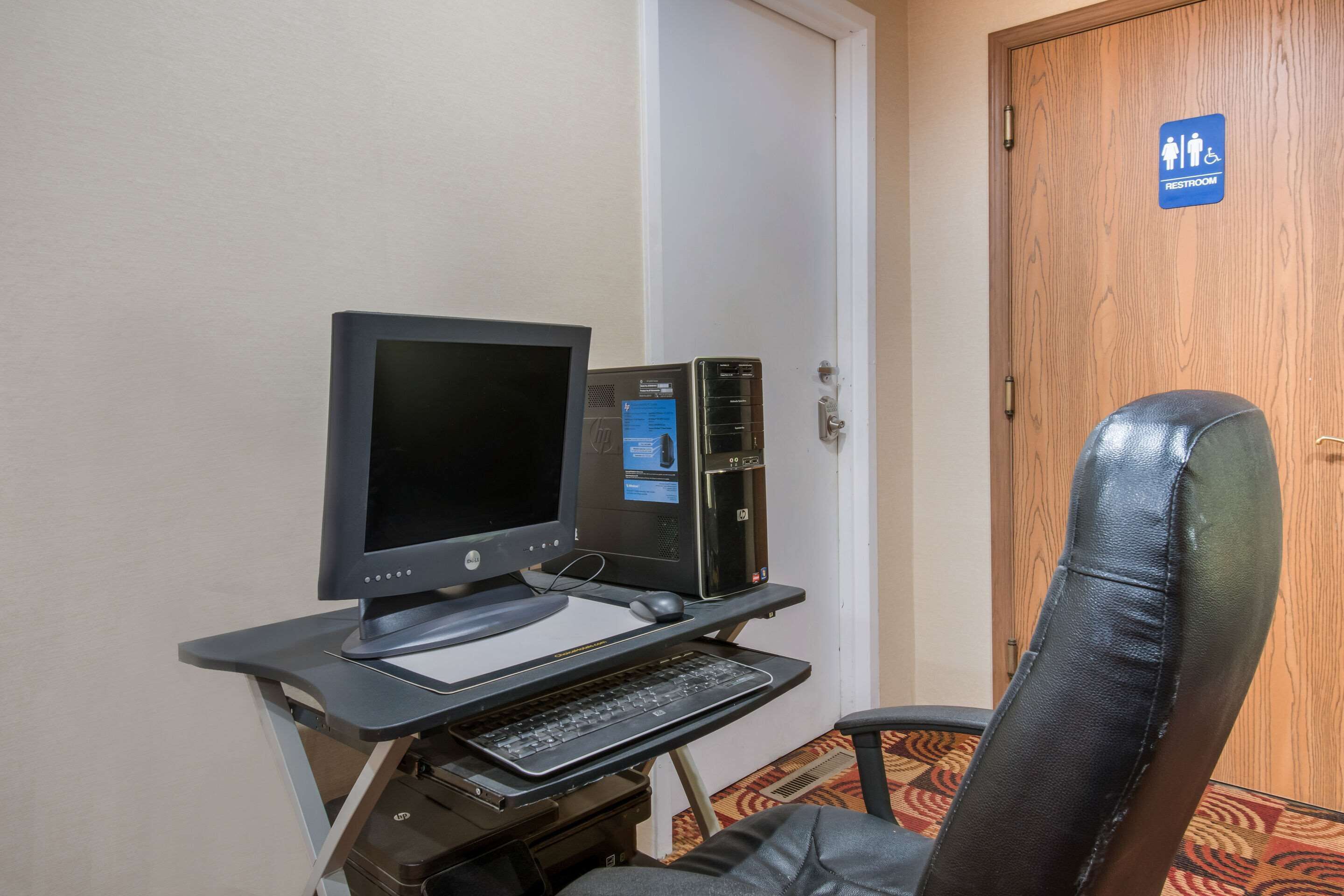 A hotel room with a computer desk, a chair, and a sign indicating a restroom.