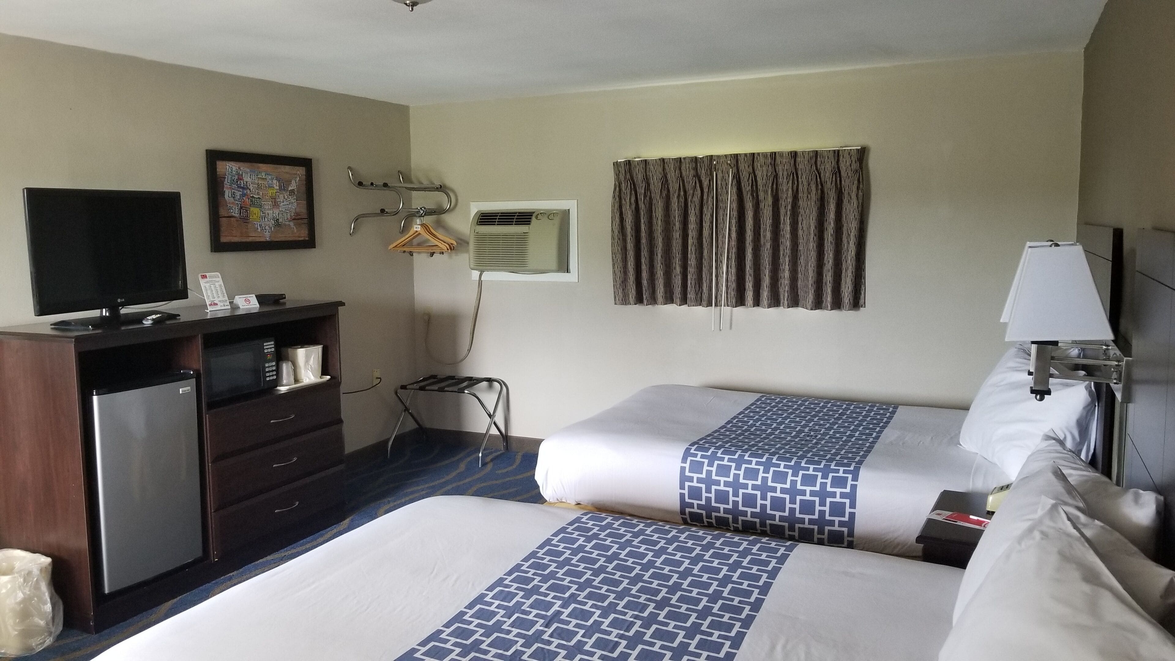 A hotel room with two beds, a desk with a computer, a television, and a window with curtains.