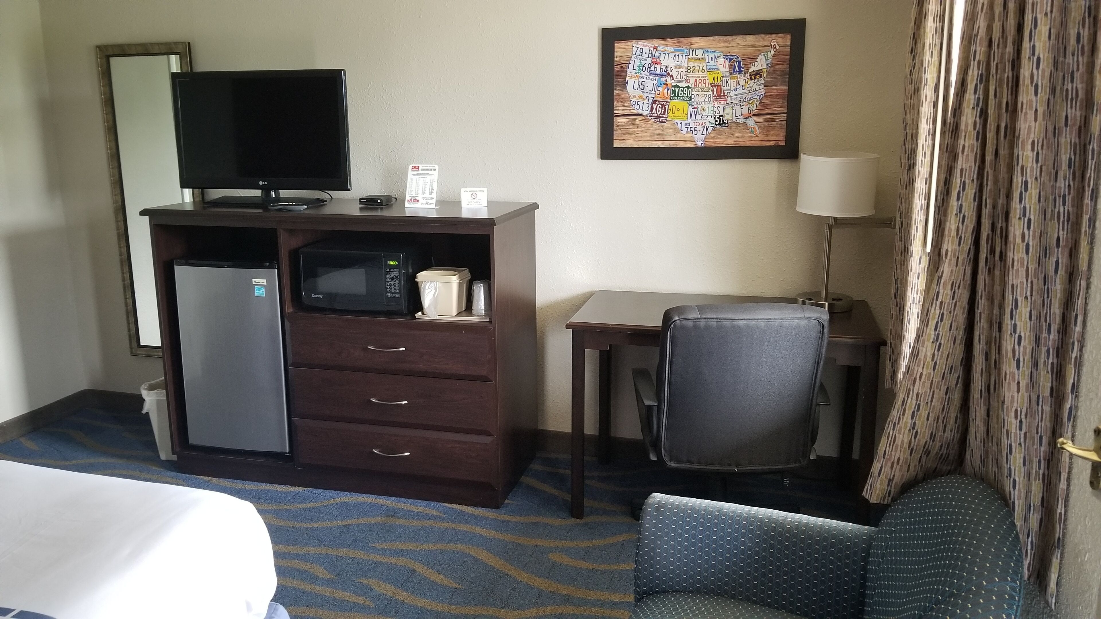Hotelkamer met een bed, een bureau, een stoel, een magnetron, een koelkast, een televisie en een kunstwerk aan de muur.