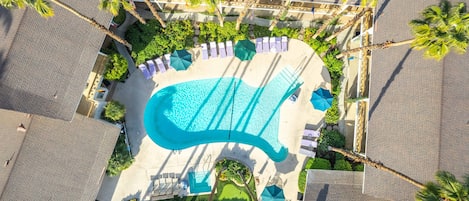 An aerial view of a resort with a swimming pool, palm trees, and lounge chairs.