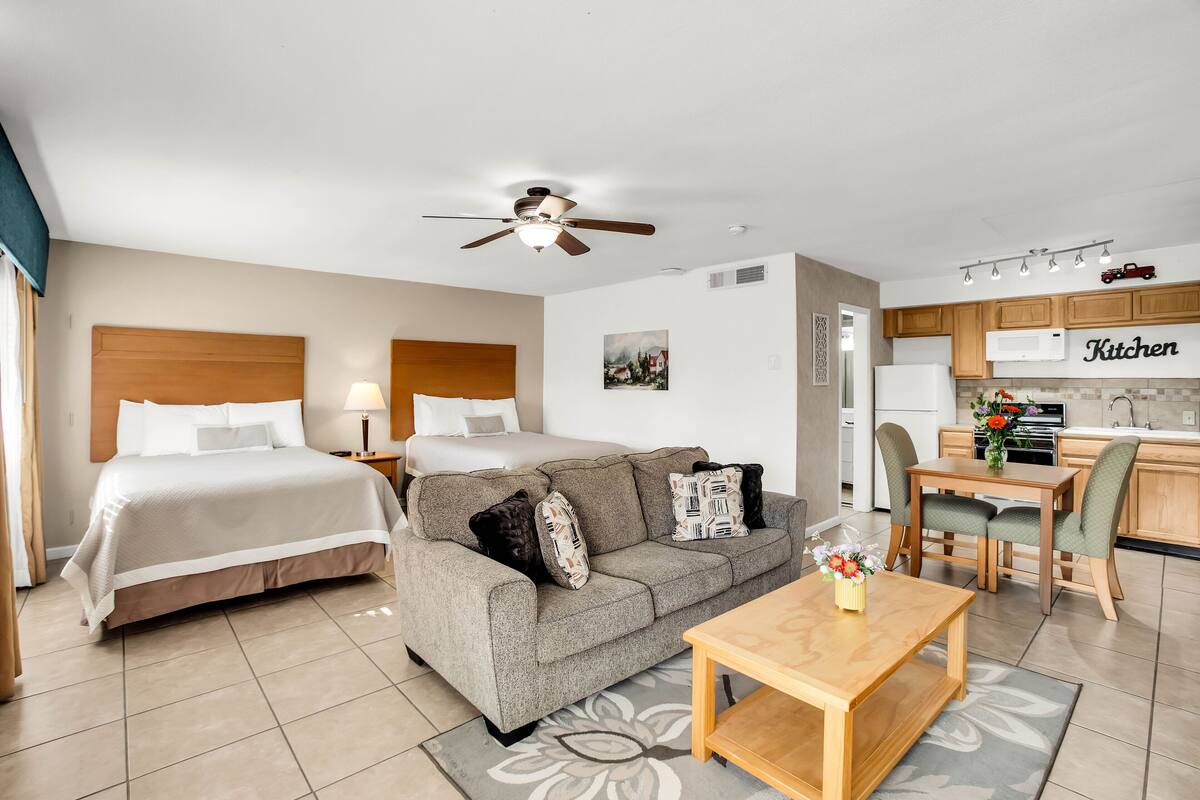 A hotel room with two beds, a sofa, a dining table, and a kitchenette.