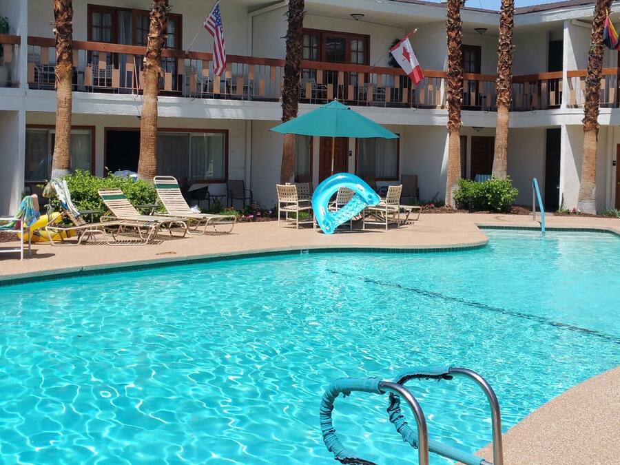 Un espace piscine d’hôtel avec des chaises longues, des parasols et une piscine à l’eau d’un bleu limpide.
