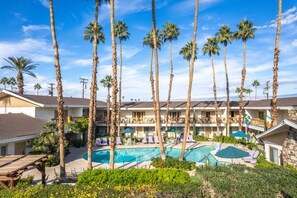 A hotel with a pool surrounded by palm trees, multiple balconies, and flags.