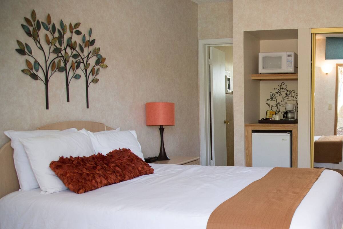 A hotel room with a bed, a desk with a microwave, a small refrigerator, and a wall-mounted artwork.