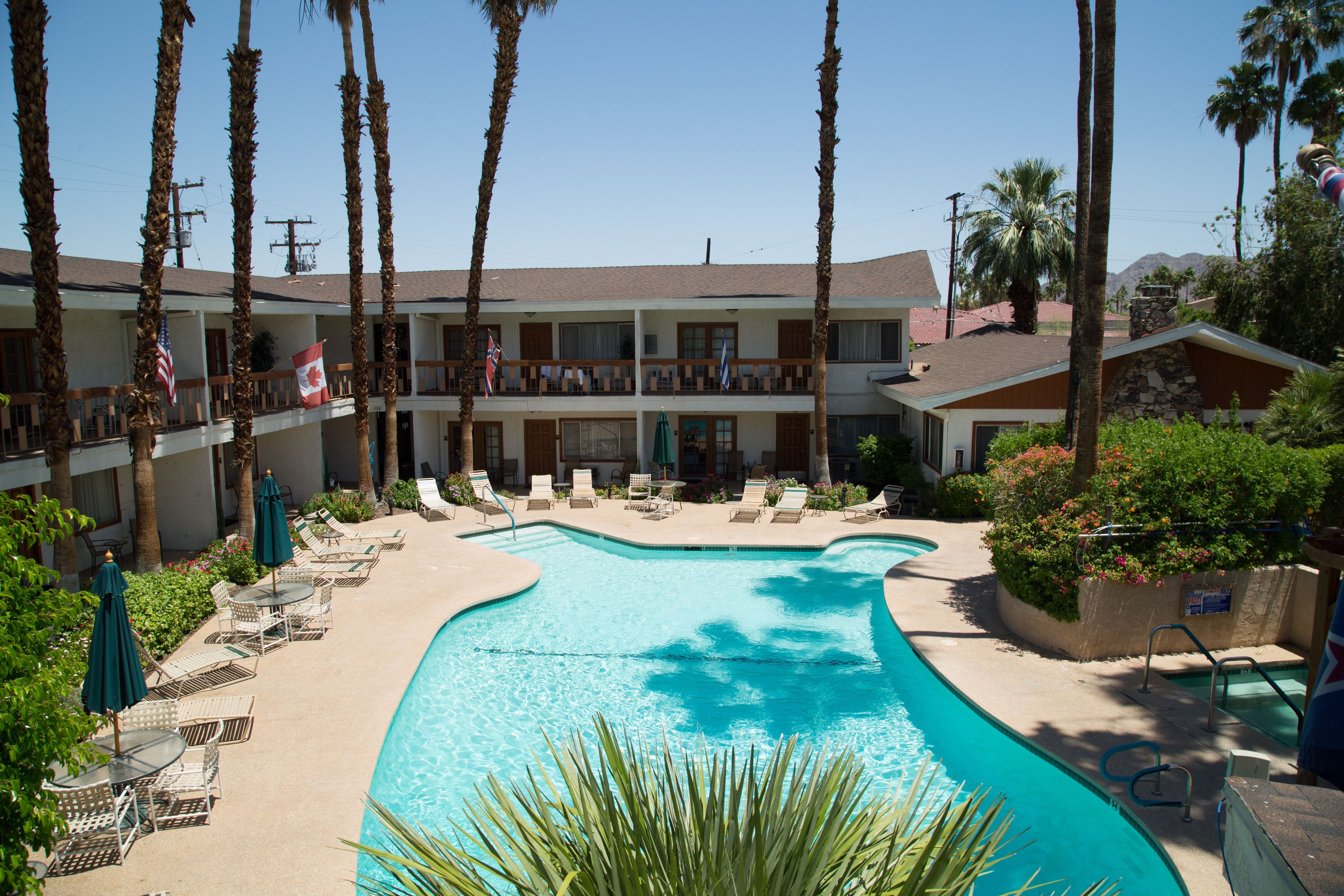 Un hotel con piscina, sillones de descanso y palmeras.