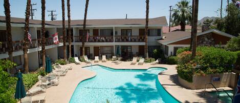 Un hotel con piscina, sillones de descanso y palmeras.