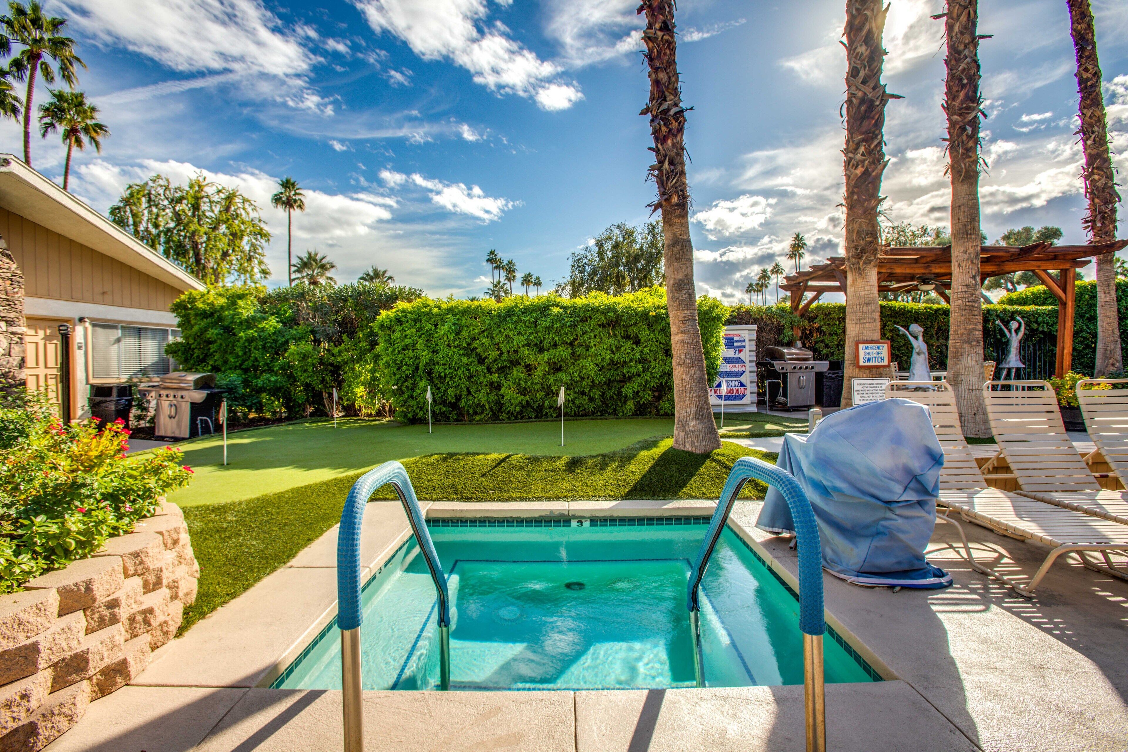 A swimming pool with a view of a backyard, palm trees, and a covered area with lounge chairs.