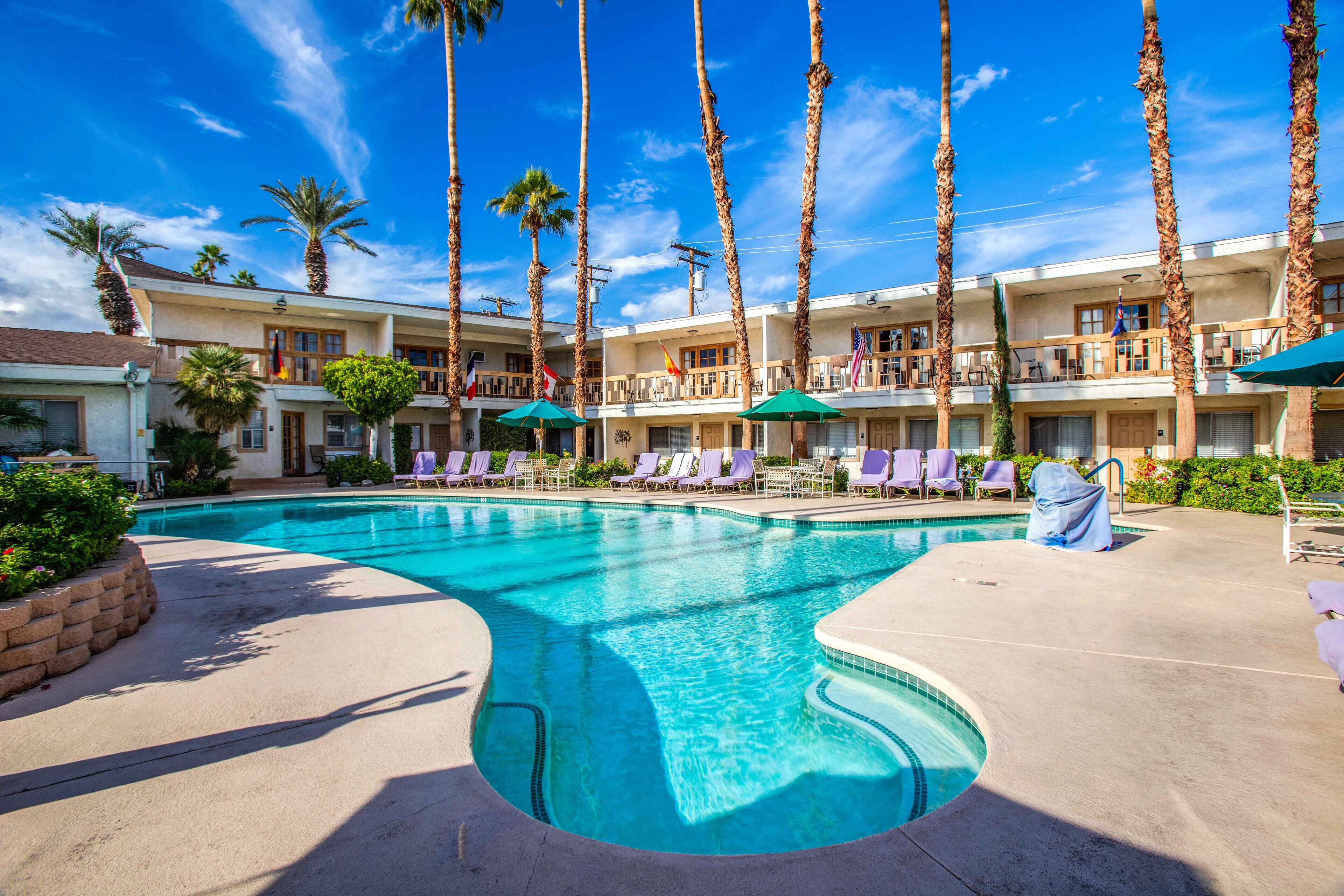 Ein Hotel mit Swimmingpool, Palmen und Liegestühlen.