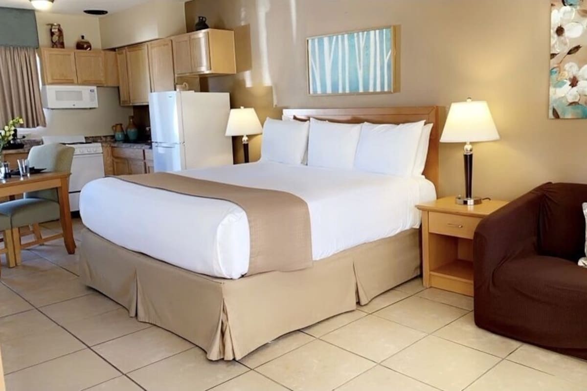 A hotel room with a bed, a desk, a chair, a sofa, and a kitchen area.