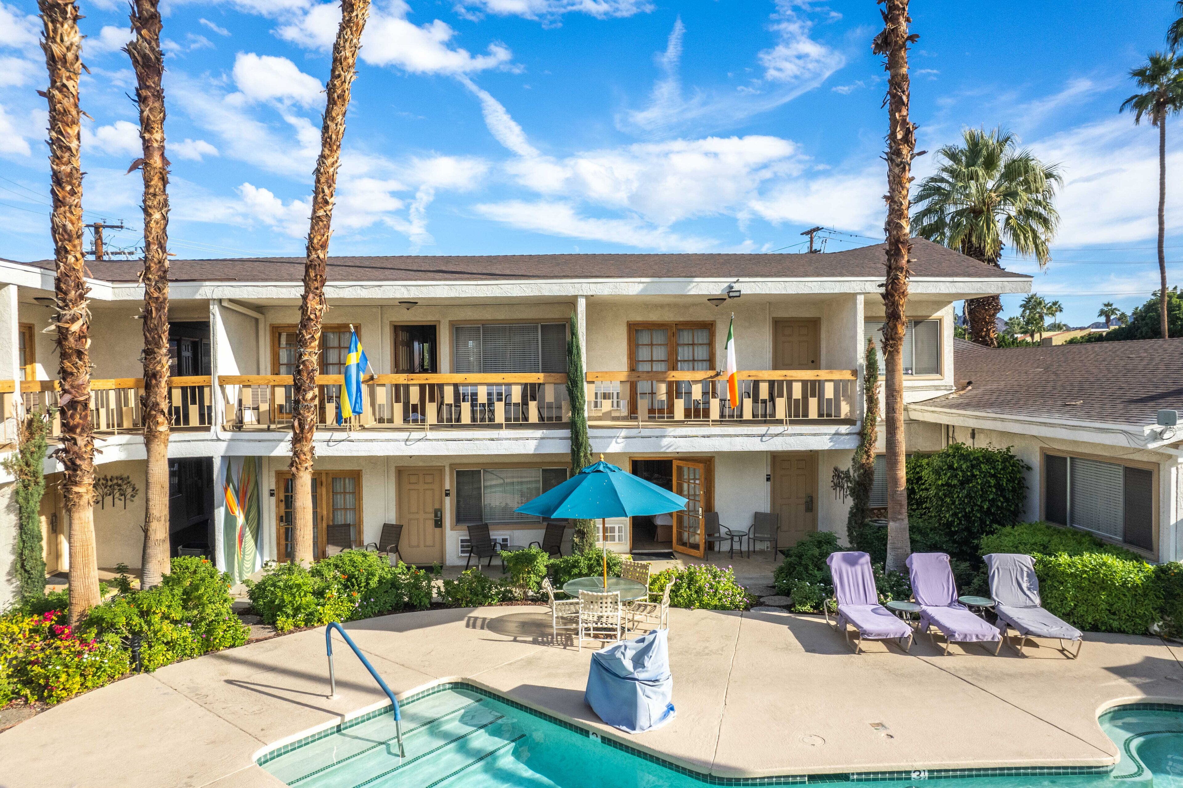 A two-story hotel with a pool, lounge chairs, and palm trees.