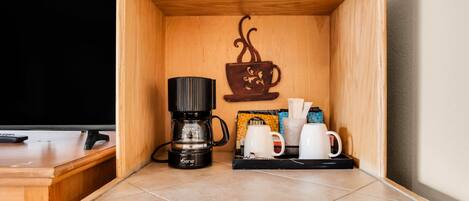 A wooden cabinet with a coffee maker, two white mugs, and a coffee cup decoration.