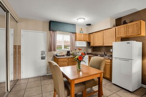 Una cocina compacta con armarios de madera, un refrigerador blanco, una mesa de comedor con sillas y un ventanal con cortinas.