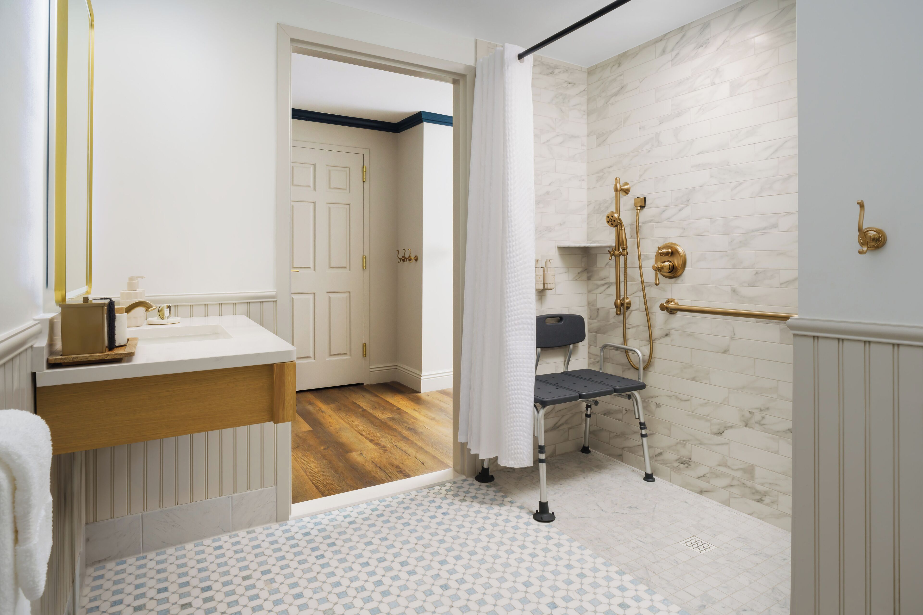 A bathroom with a white sink, a shower with a gold showerhead, and a wheelchair-accessible shower chair.