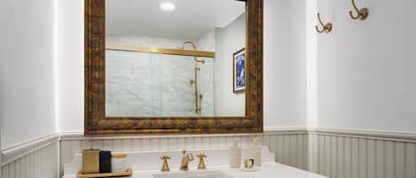 A bathroom with a large mirror, a white sink, and gold fixtures.