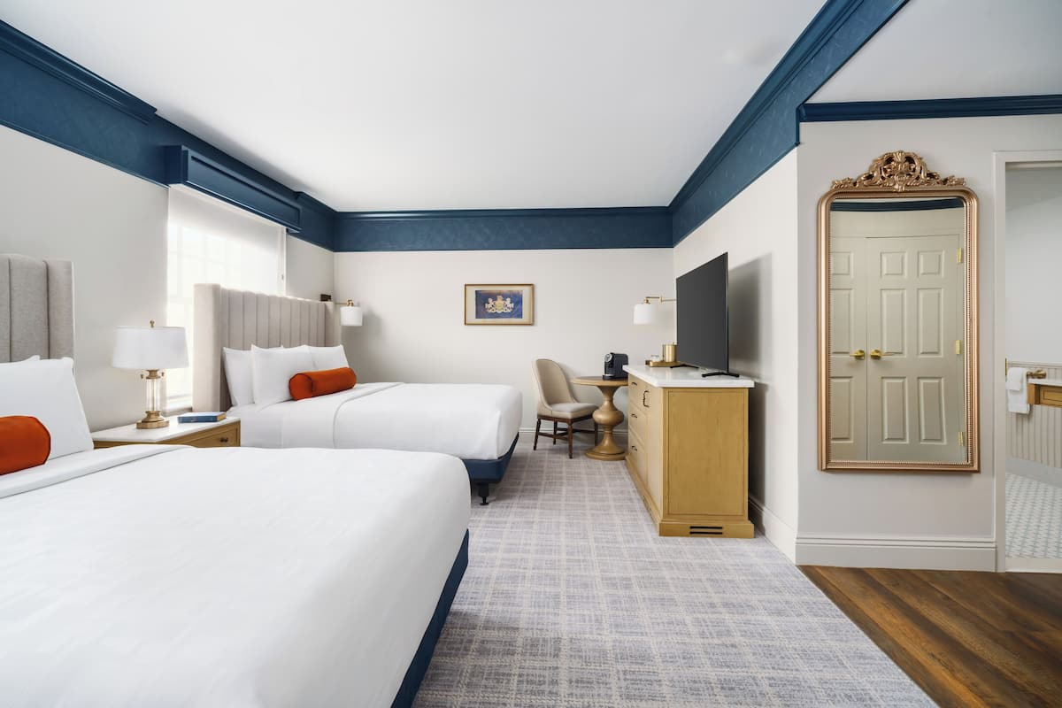 A hotel room with two beds, a desk, a television, and a door.