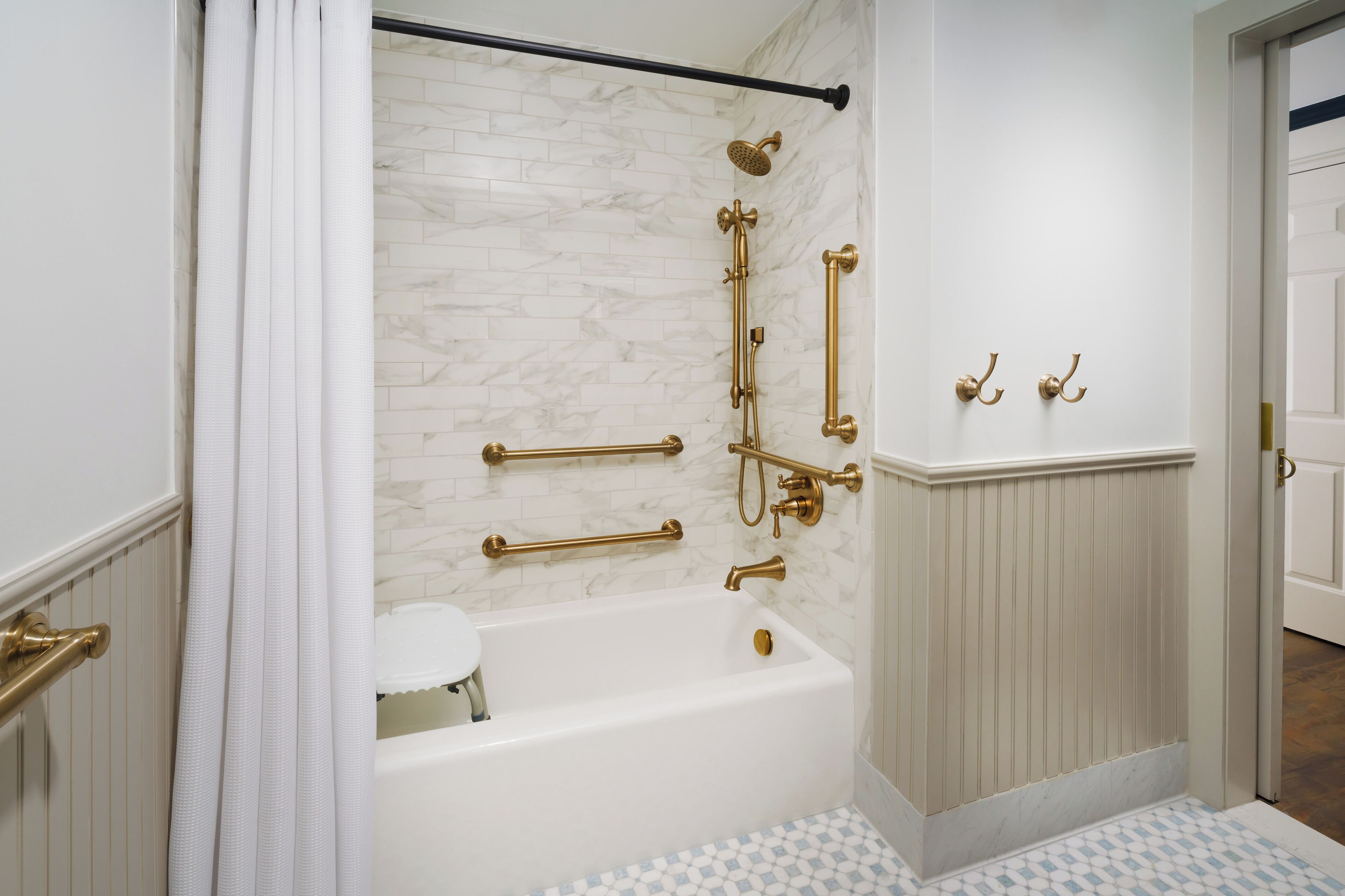 A bathroom with a white bathtub, marble wall, gold fixtures, and a checkered floor pattern.