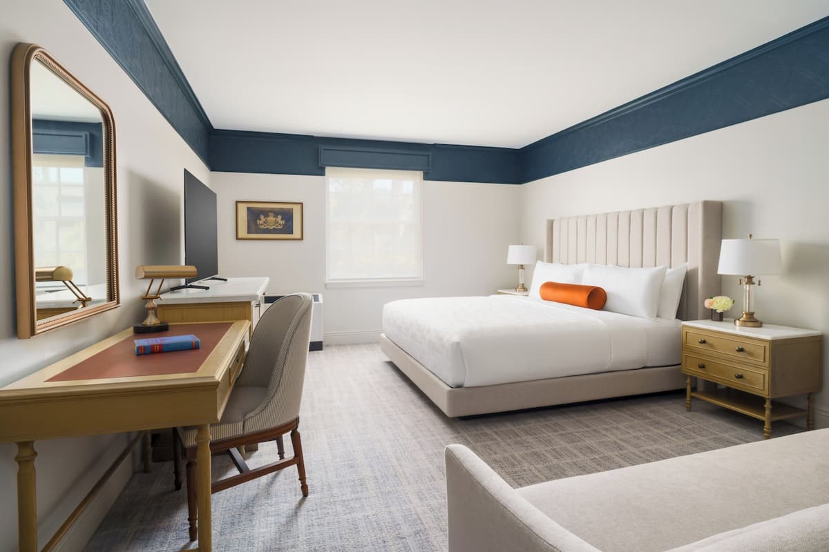 A hotel room with a bed, desk, chair, bedside tables, and a large mirror.