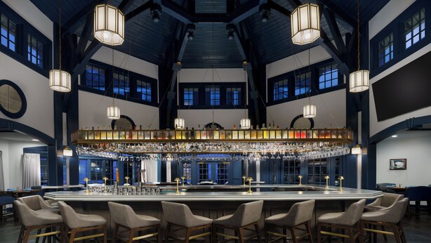 A spacious bar area with multiple seating arrangements and a high ceiling with exposed beams.