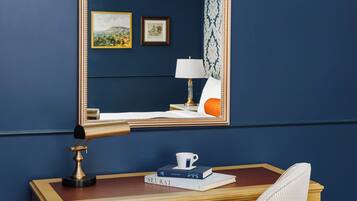 A wooden desk with a mirror, a lamp, and a chair. There are books and a cup on the desk.