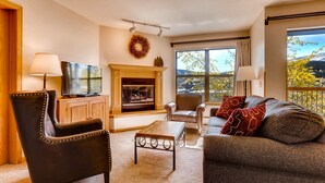 A living room with a fireplace, a television, a sofa, and a view of the outdoors. - River Mountain Lodge (Breckenridge)