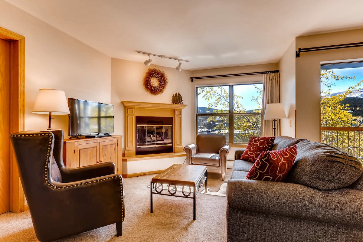 A living room with a fireplace, a television, a sofa, and a view of the outdoors.