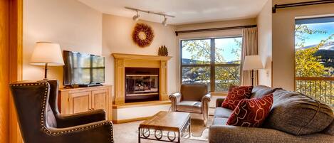 Una sala de estar con chimenea, televisor, sofá y vistas al exterior.