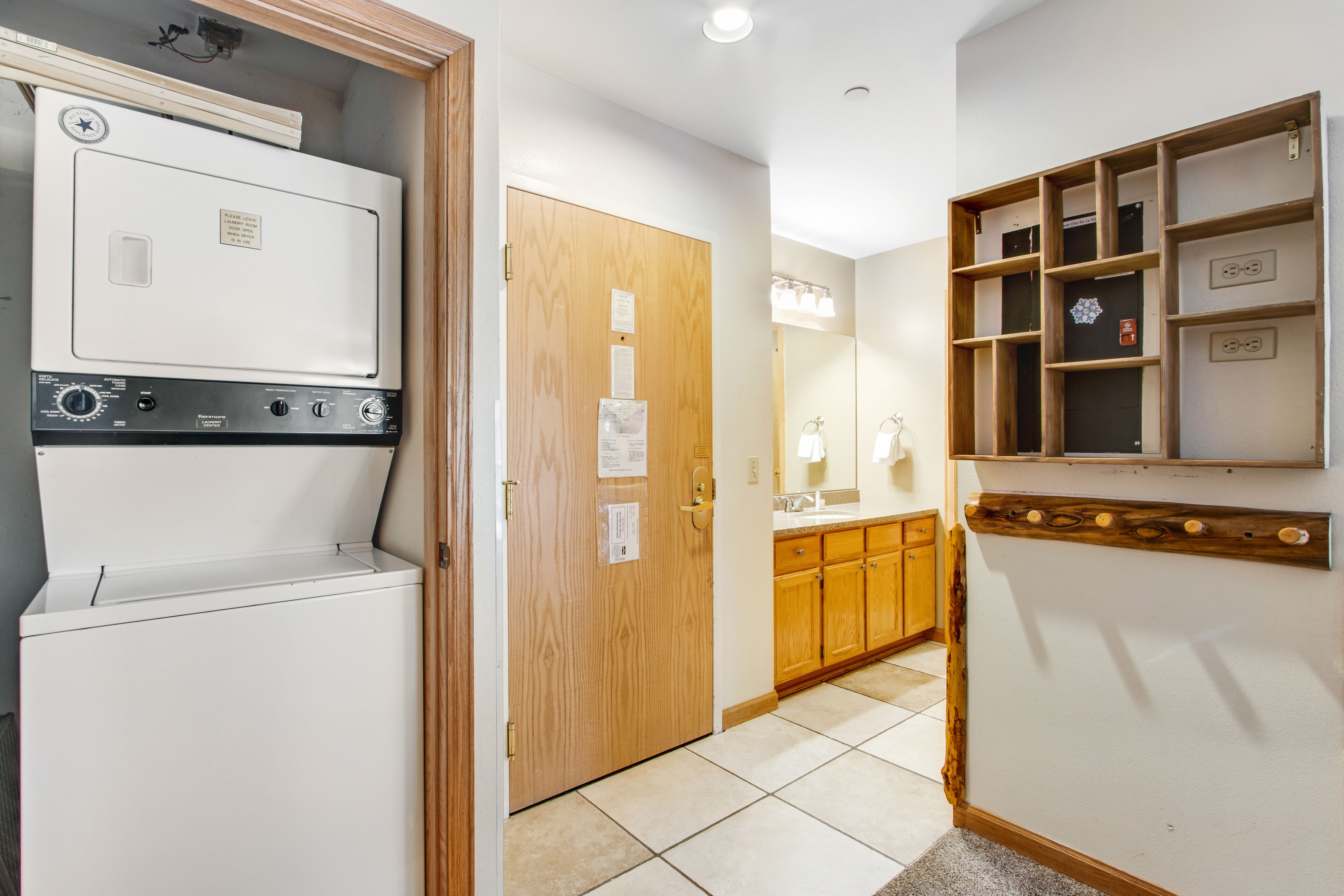 A laundry room with a Kenmore washer and dryer, a wooden door, and a bathroom with a sink and mirror.