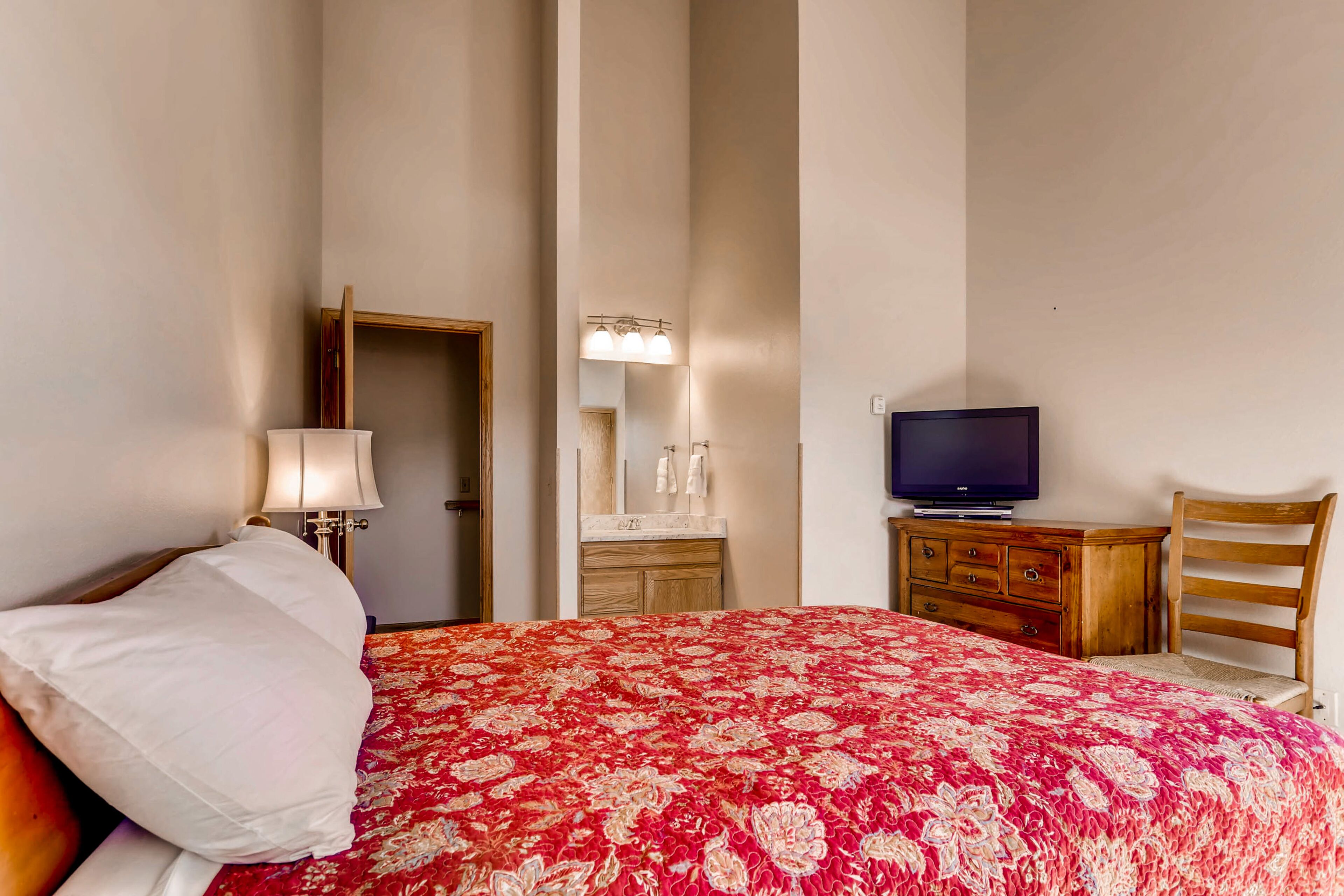 A bedroom with a bed, a television, a wooden dresser, and a mirror.