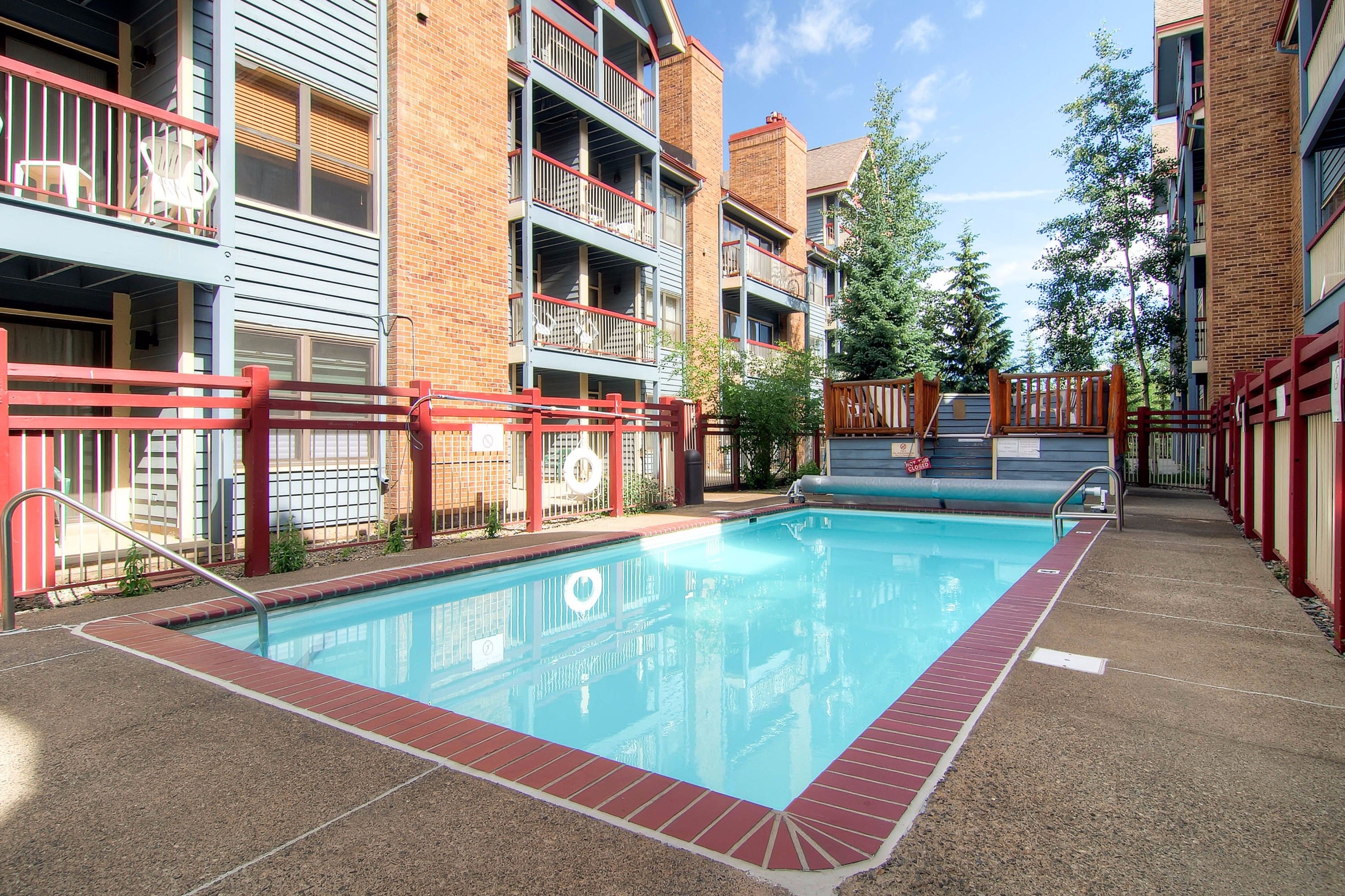 A swimming pool with a red border, surrounded by multi-story buildings with balconies and a brick facade.