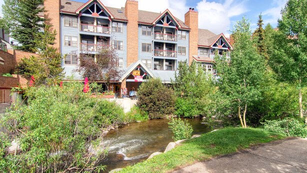 A multi-story hotel with balconies, a small stream in front, and surrounded by greenery. - River Mountain Lodge (Breckenridge)