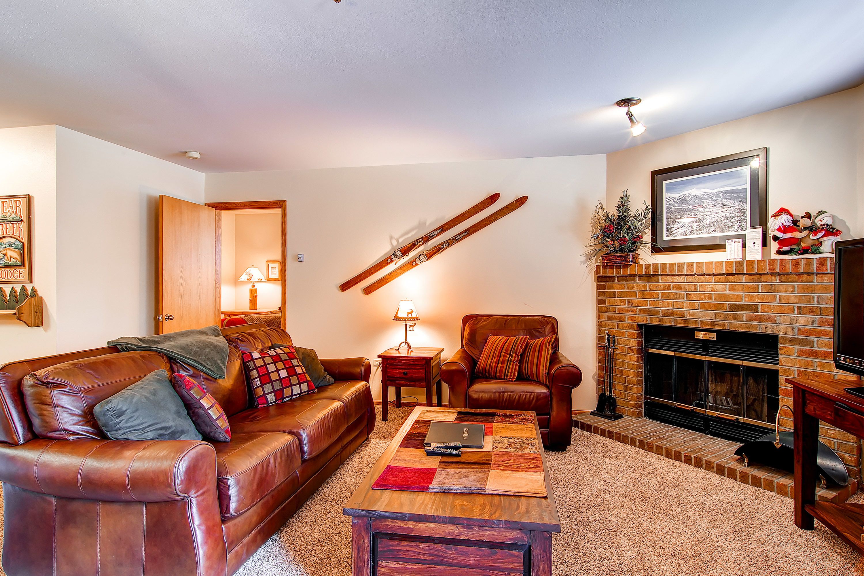 A cozy living room with a leather sofa, a coffee table, a fireplace, and a mounted ski rack.