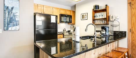 A kitchen with wooden cabinets, a black refrigerator, a microwave, a sink, and a bar stool.