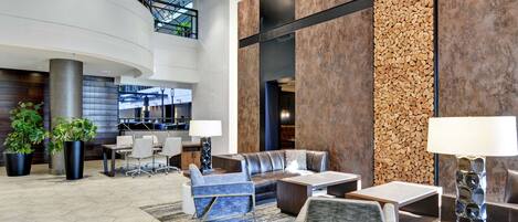 A spacious lobby with a curved staircase, seating area with sofas and chairs, and a large wall with a textured pattern.