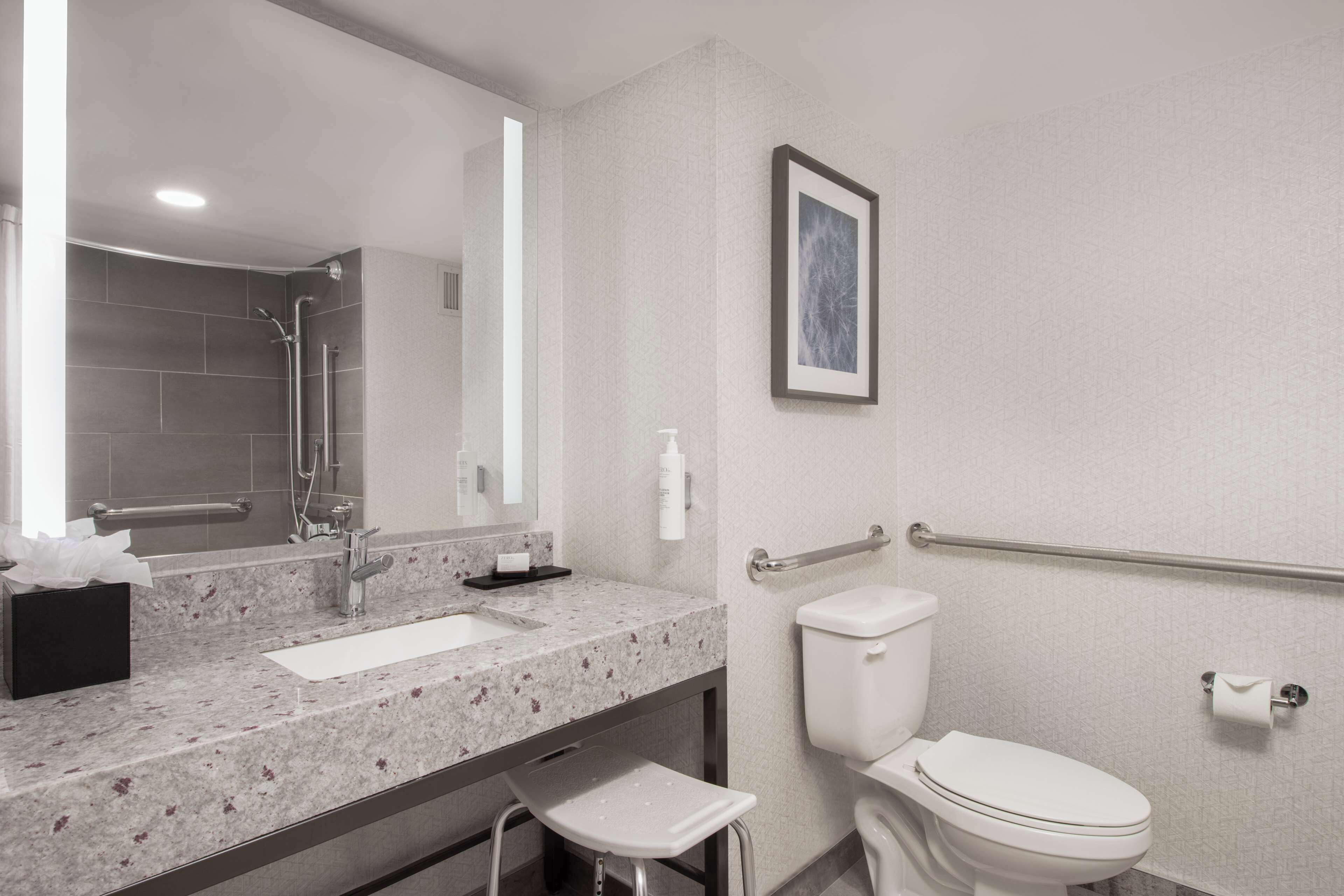 A modern bathroom with a sink, mirror, toilet, and a small step stool.