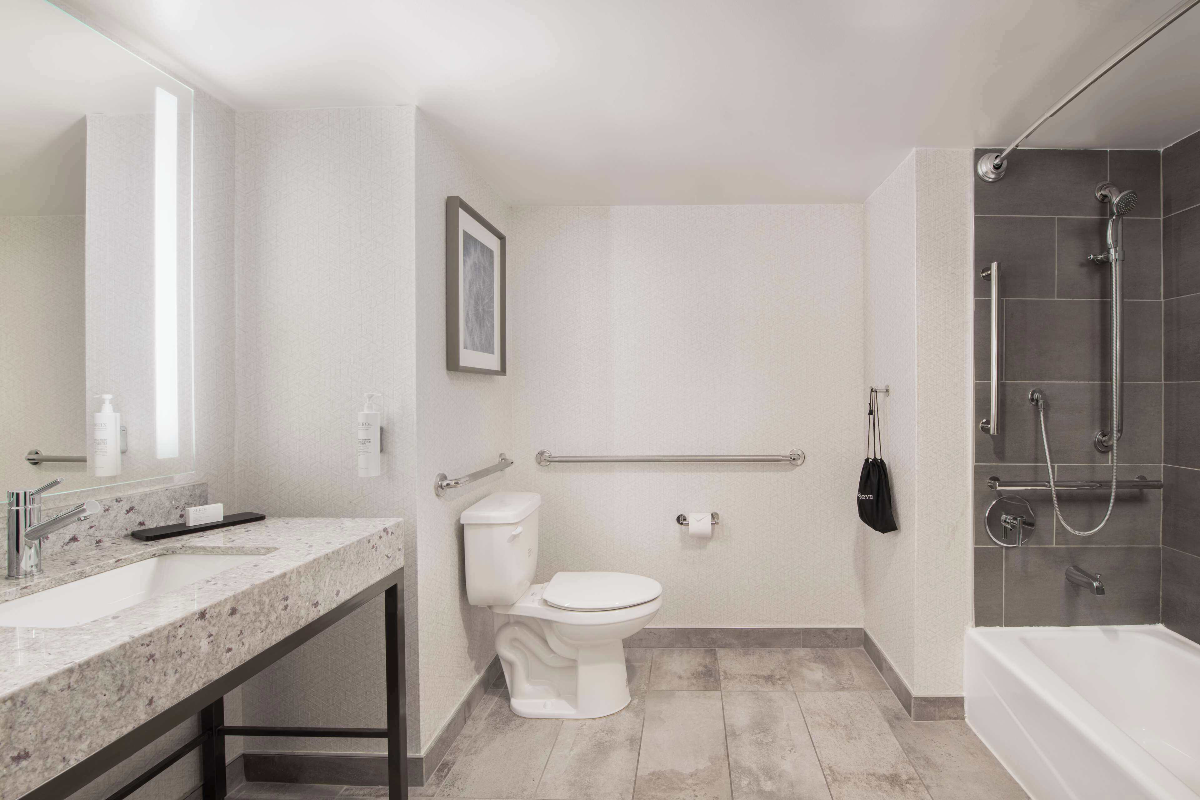 A modern bathroom with a marble countertop, a white toilet, a shower with a handheld showerhead, and a grab bar for safety.