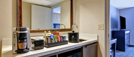 Una kitchenette de hotel con cafetera, microondas y una estación de café con diversas bebidas.