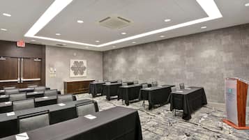 A conference room with rows of tables and chairs, a podium, and an exit sign.