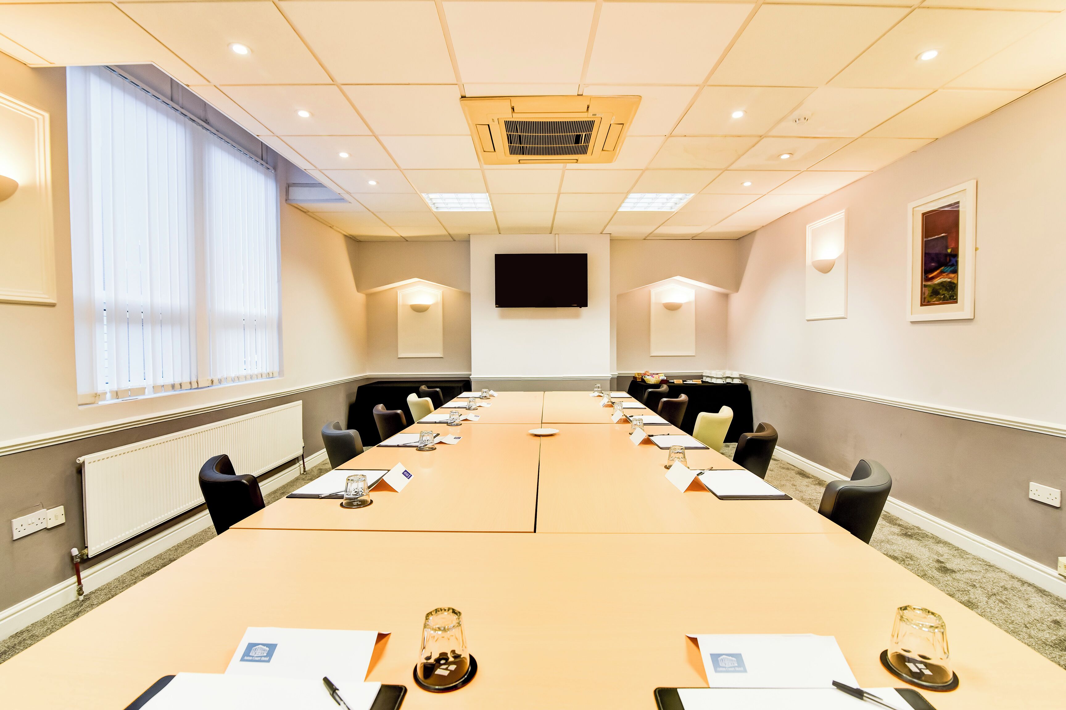 A conference room with a long table, chairs, a projector screen, and a window with blinds.